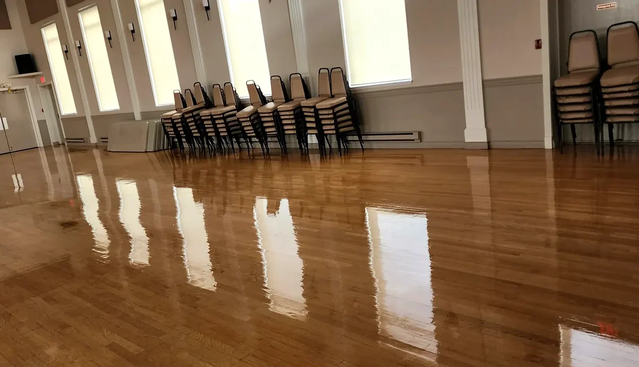 Polished banquet hall hardwood floor reflecting tall windows and stacked chairs