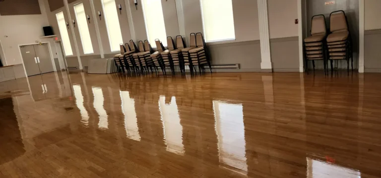 Polished banquet hall hardwood floor reflecting tall windows and stacked chairs