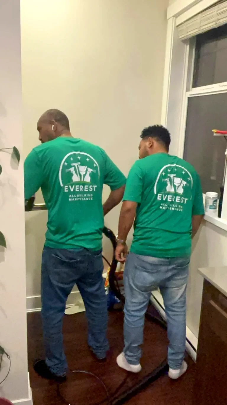 Two Everest crew members with a carpet extraction hose in a narrow hallway