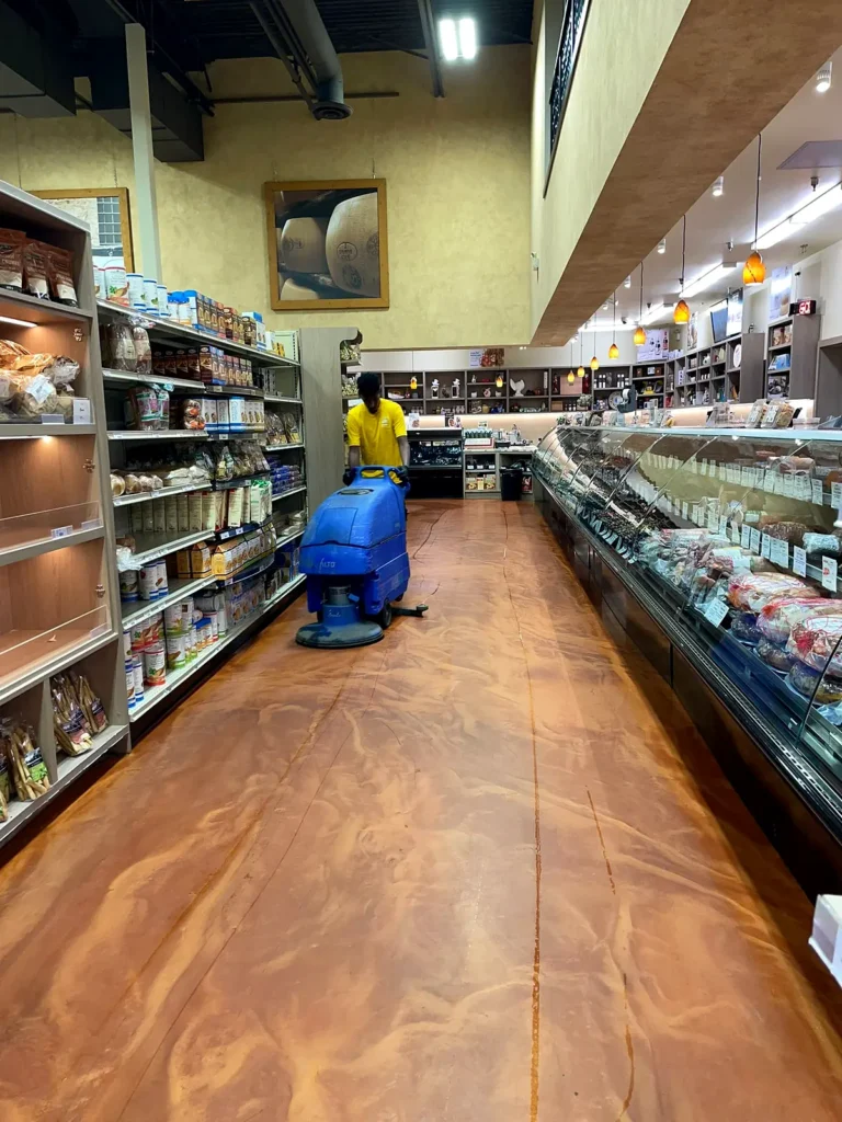 Crew member operating a blue auto scrubber down a grocery store aisle