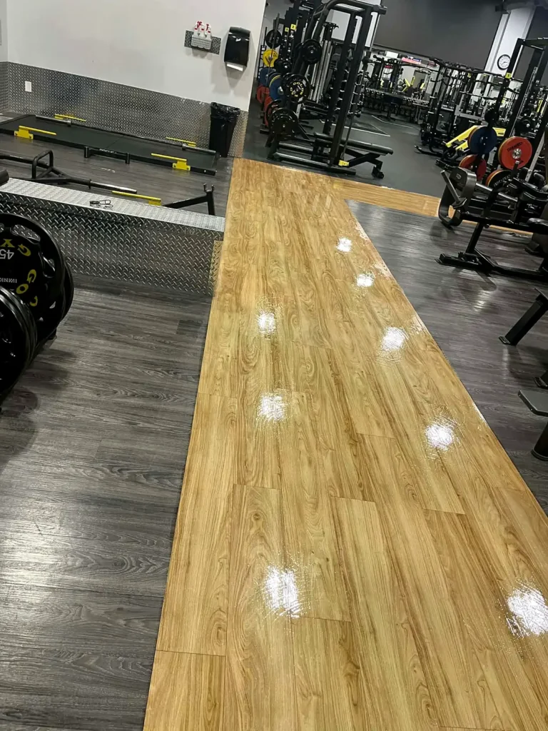 Glossy wood-look floor runway between fitness equipment in a gym