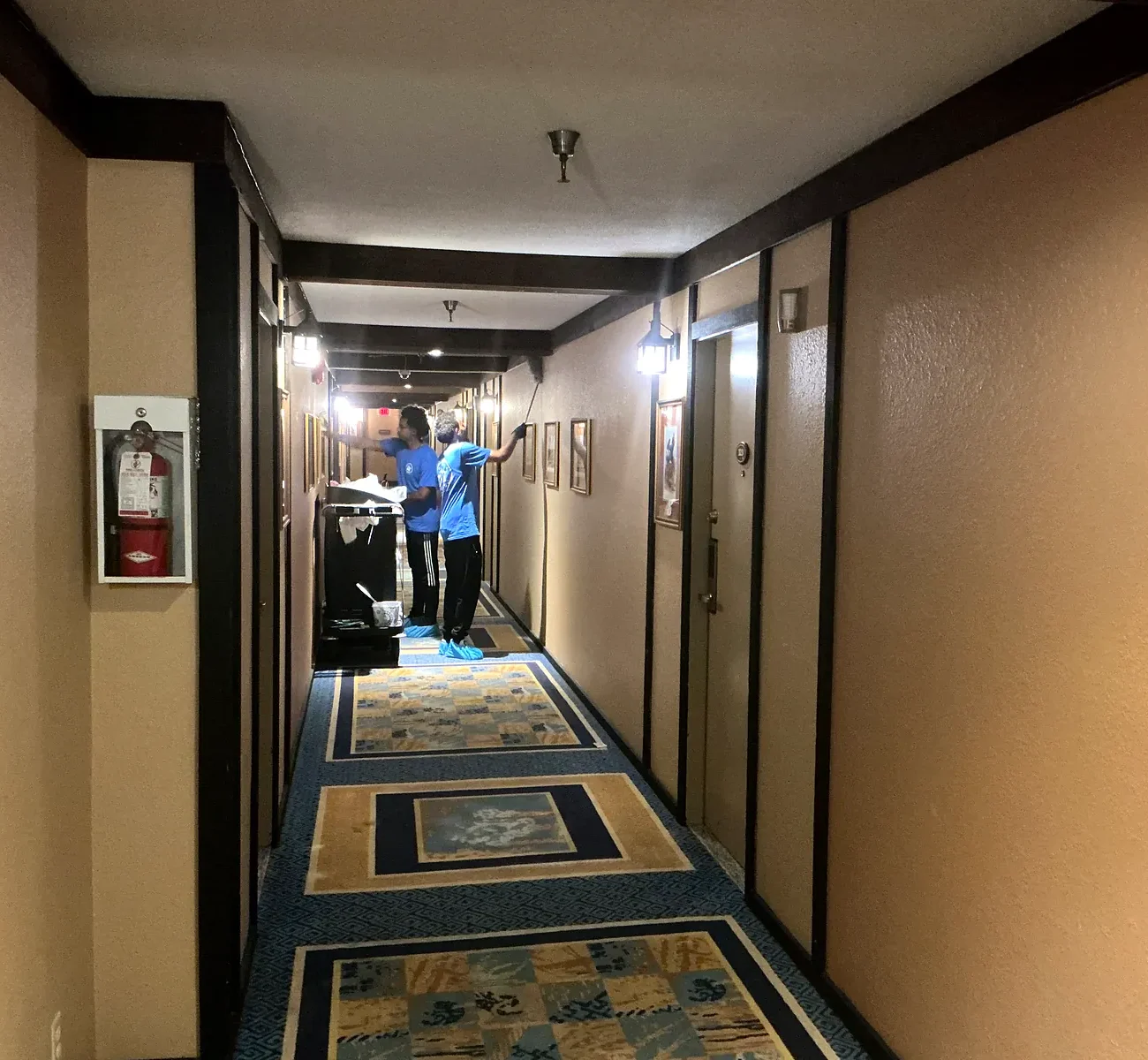Cleaner with equipment on a patterned carpet in a long hotel hallway