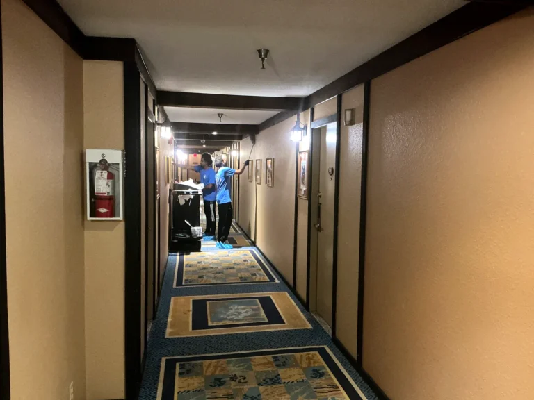Cleaner with equipment on a patterned carpet in a long hotel hallway