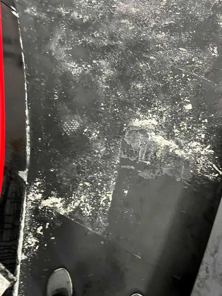 White construction dust on a black rubber floor along curved rink boards