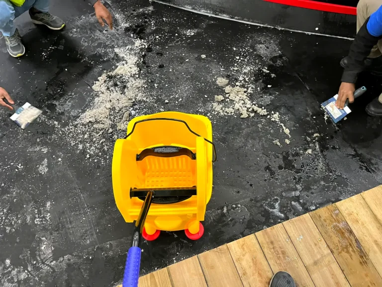 Construction dust and debris on the rink floor beside a mop bucket, before cleaning