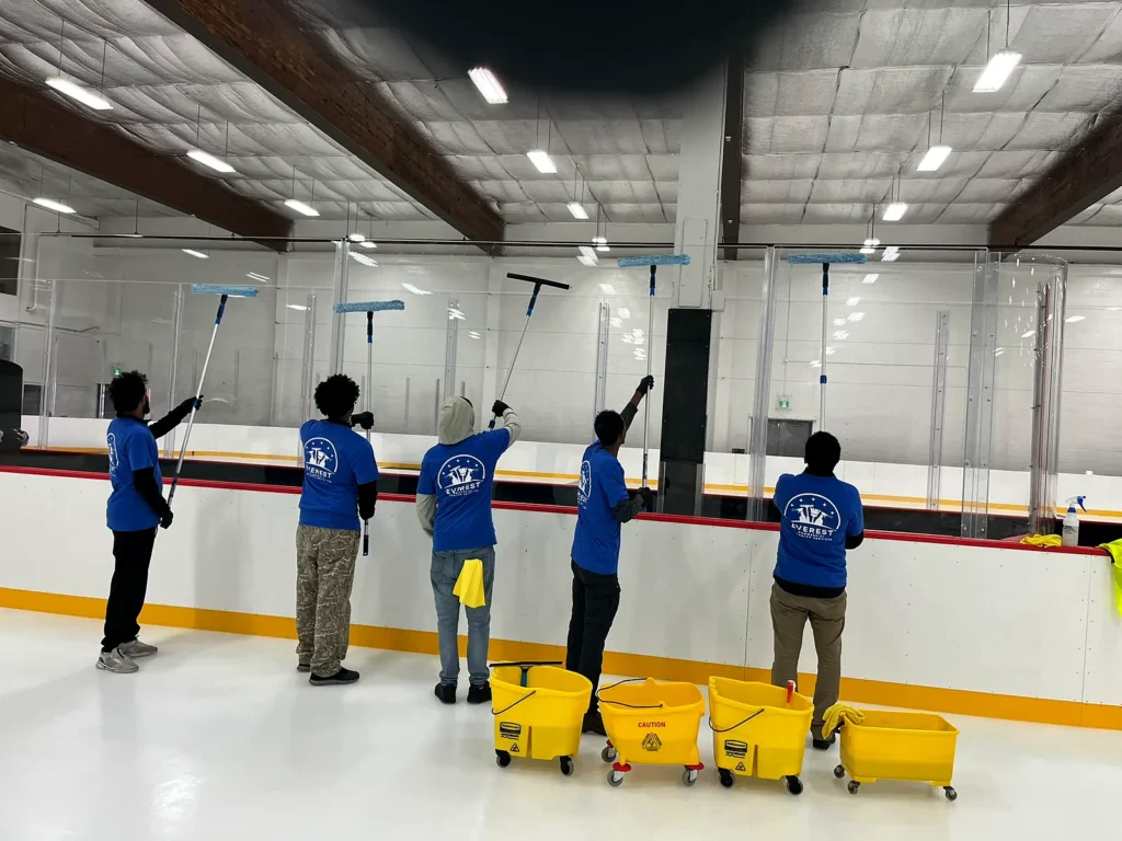 Crew of five using extension poles to clean the glass above the rink boards