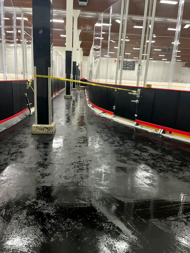 Wet black rubber floor beside the rink boards while being washed