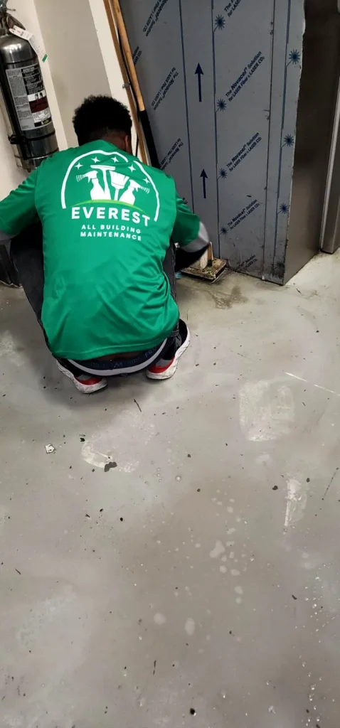 Everest crew member crouching to clean a grey commercial kitchen floor