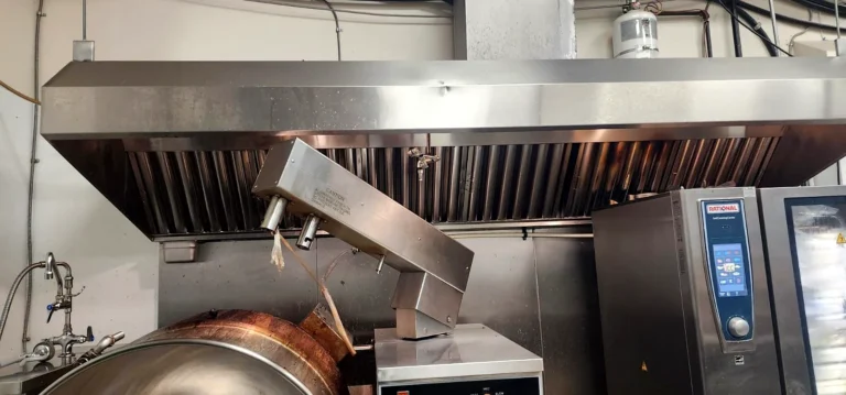 Stainless steel exhaust hood above a steam kettle and combi oven in a commercial kitchen