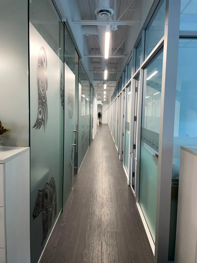 Long office corridor with frosted glass walls and a clean dark floor
