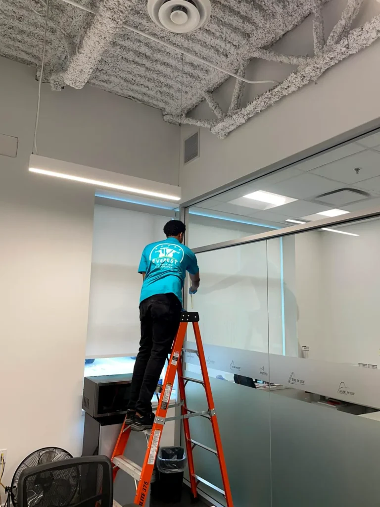 Everest crew member on a ladder cleaning glass partition walls in a modern office