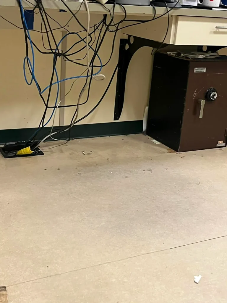 Before: dull, dirty VCT floor beside a desk with cables and a safe