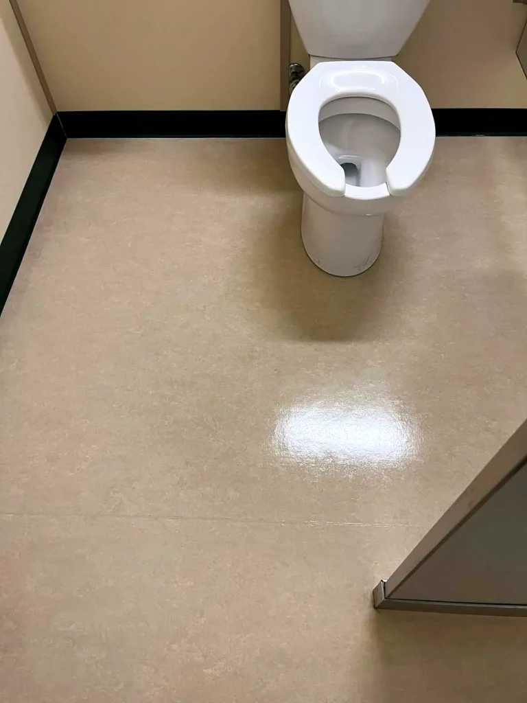 Glossy waxed floor in a washroom stall beside the toilet