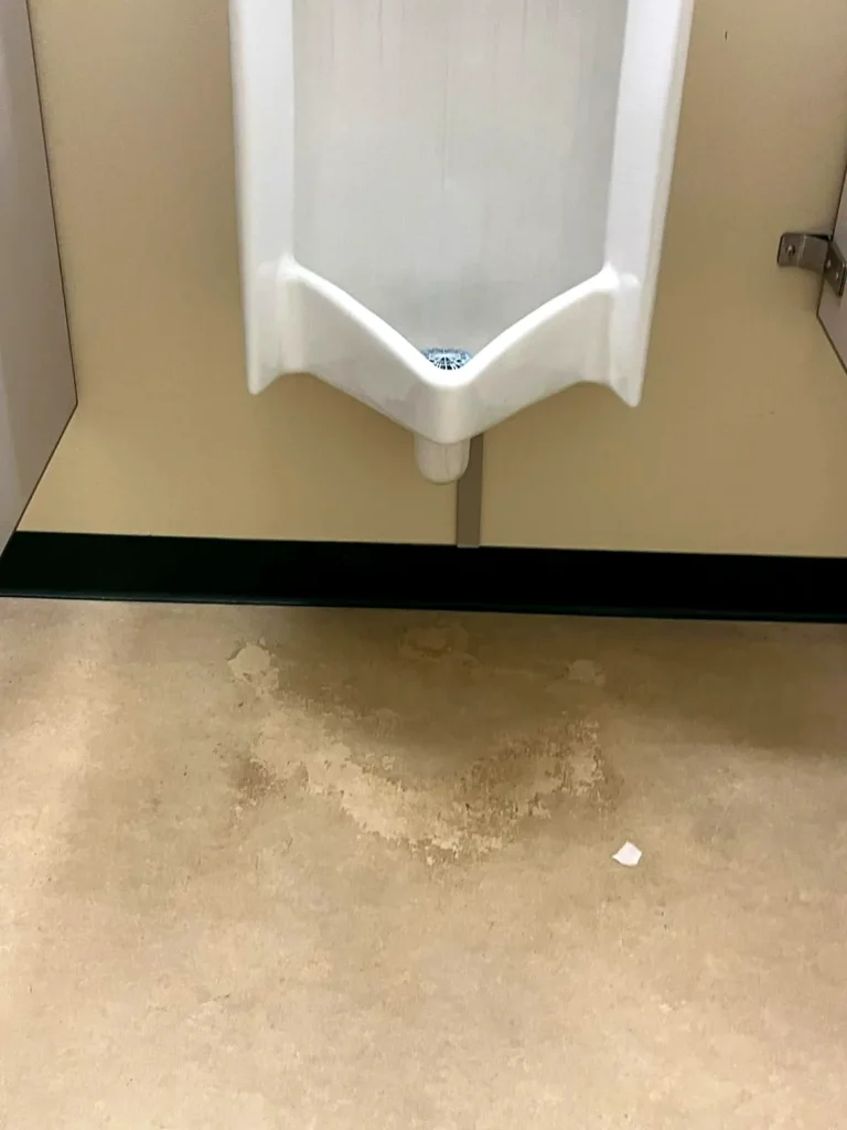 Stained, dull vinyl floor beneath a urinal before stripping and waxing